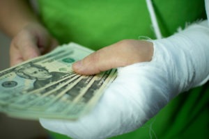 hand wrapped in gauze holding twenty-dollar bills