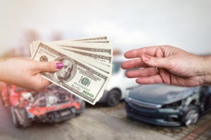 hands exchanging money with damaged cars in background