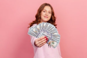 satisfied young woman holding wad of hundreds