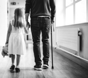 Man walking with a cane alongside his young daughter