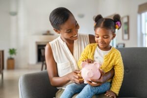 black mom and her daughter with piggy bank
